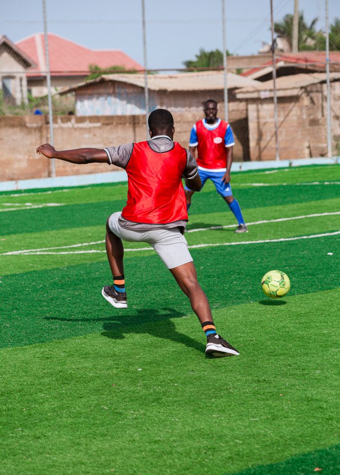 Two men playing soccer on an outdoor field, engaging in action sports with vibrant jerseys.